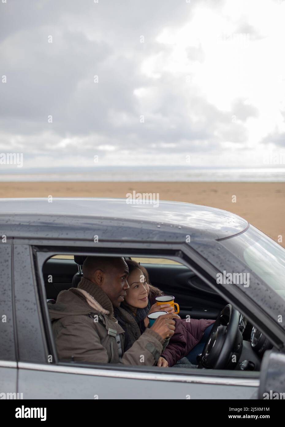 Happy couple drinking coffee in car on winter beach Stock Photo