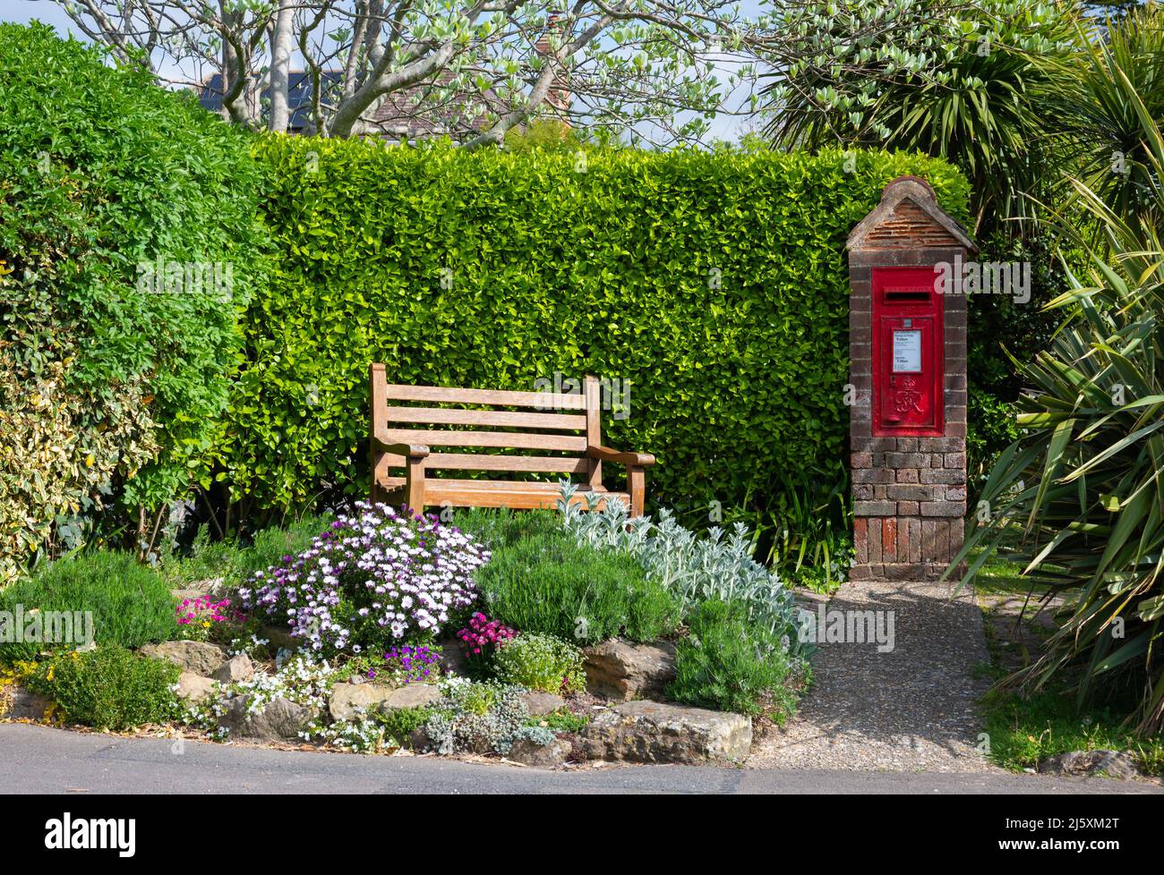 Rectangular red Royal Mail post box or letter box installed in a brick pillar next to wooden bench as a nice please to sit in West Sussex, England, UK Stock Photo
