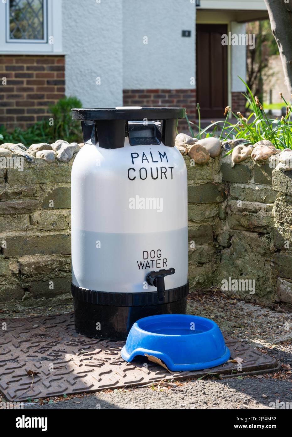 Water bowl and refilling water container left outside a residential home for dogs to drink water while walking past in England, UK. Stock Photo