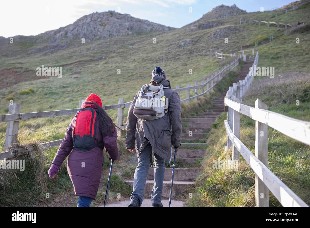 Couple with backpacks hiking up stairs on cliff Stock Photo
