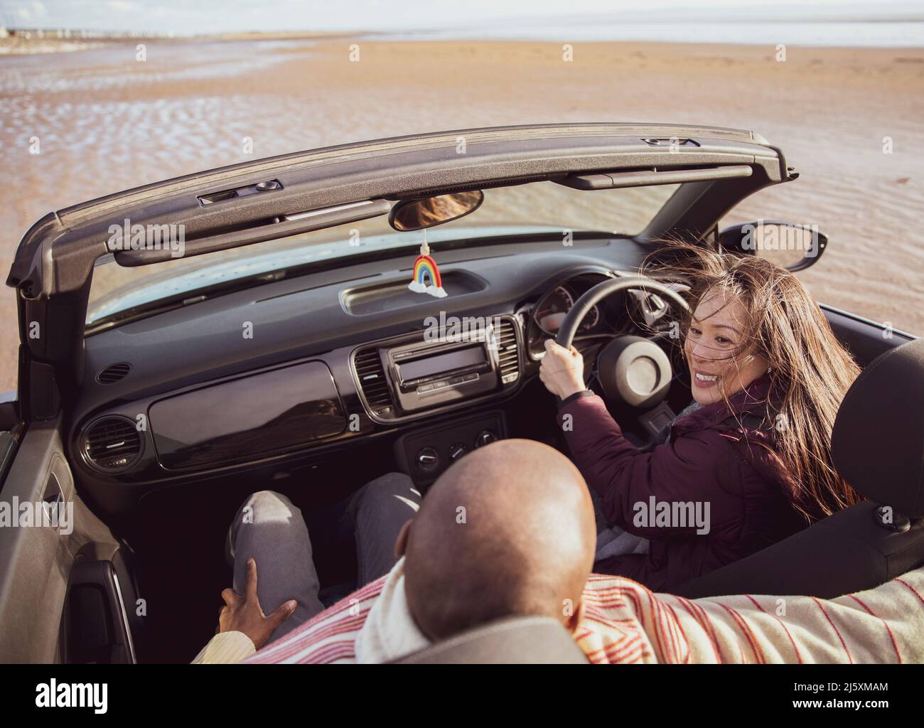 Happy couple driving convertible on sunny beach Stock Photo