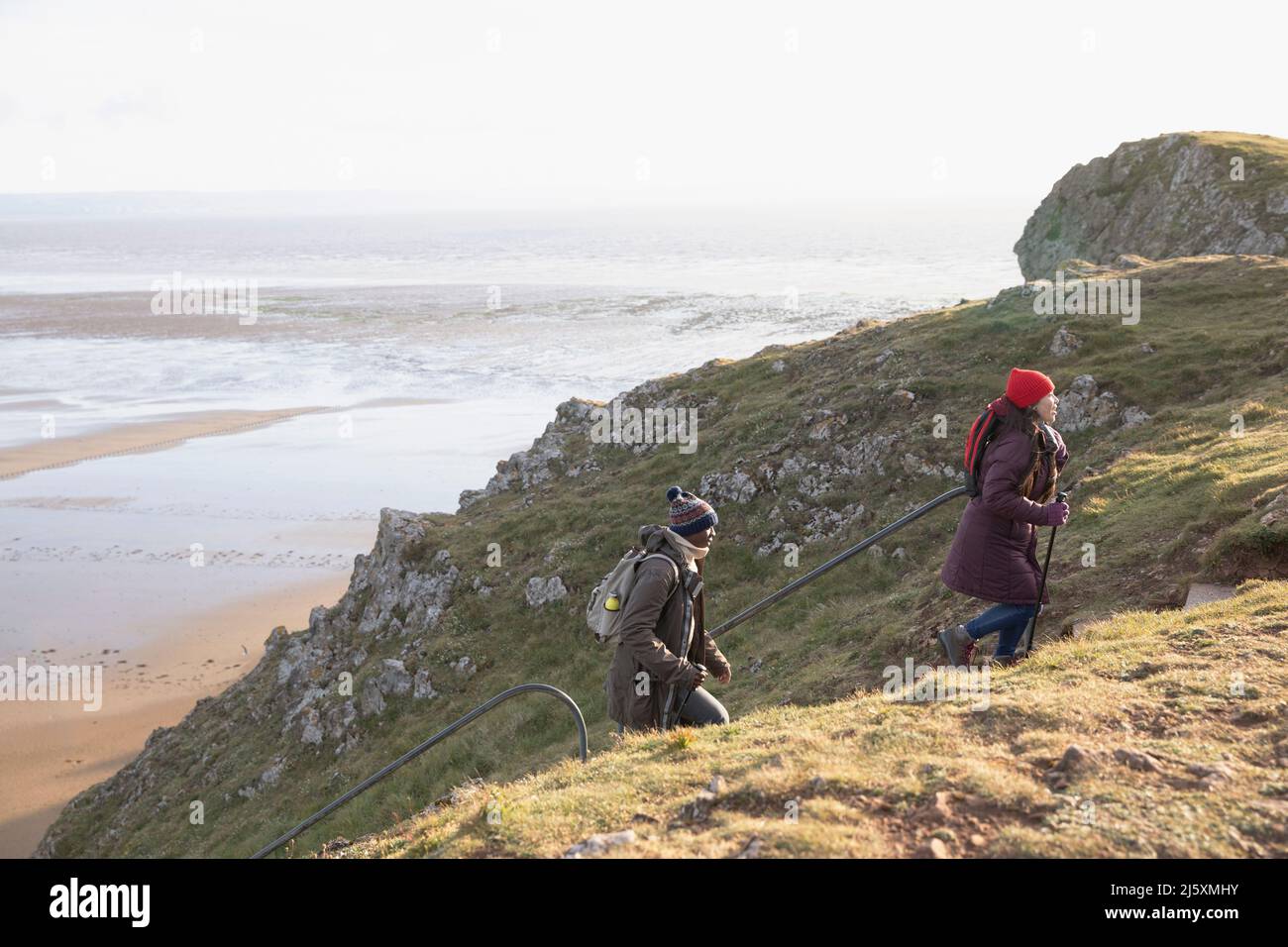 Hiker couple climbing steps on cliff above ocean beach Stock Photo