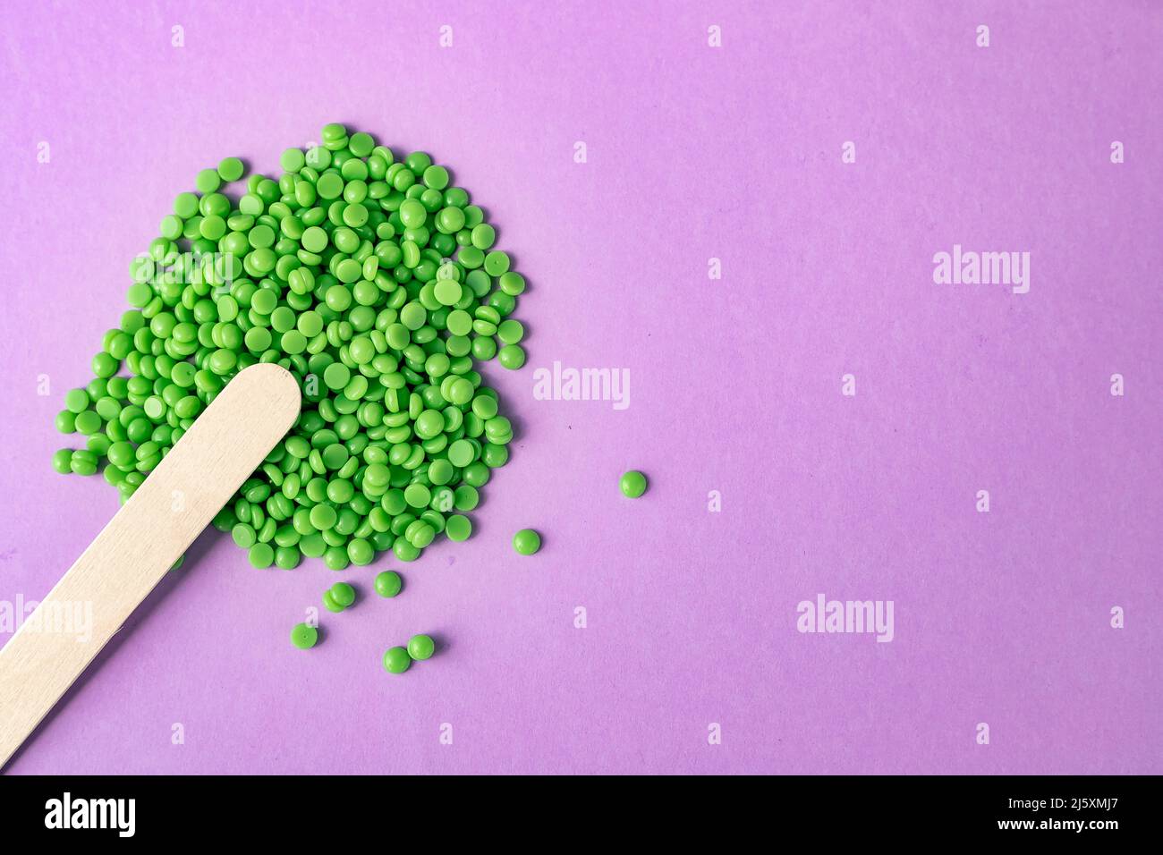 Beautiful green wax granules for depilation, and wooden spatulas on a pink background. Epilation, depilation, removal of unwanted hair. View from abov Stock Photo