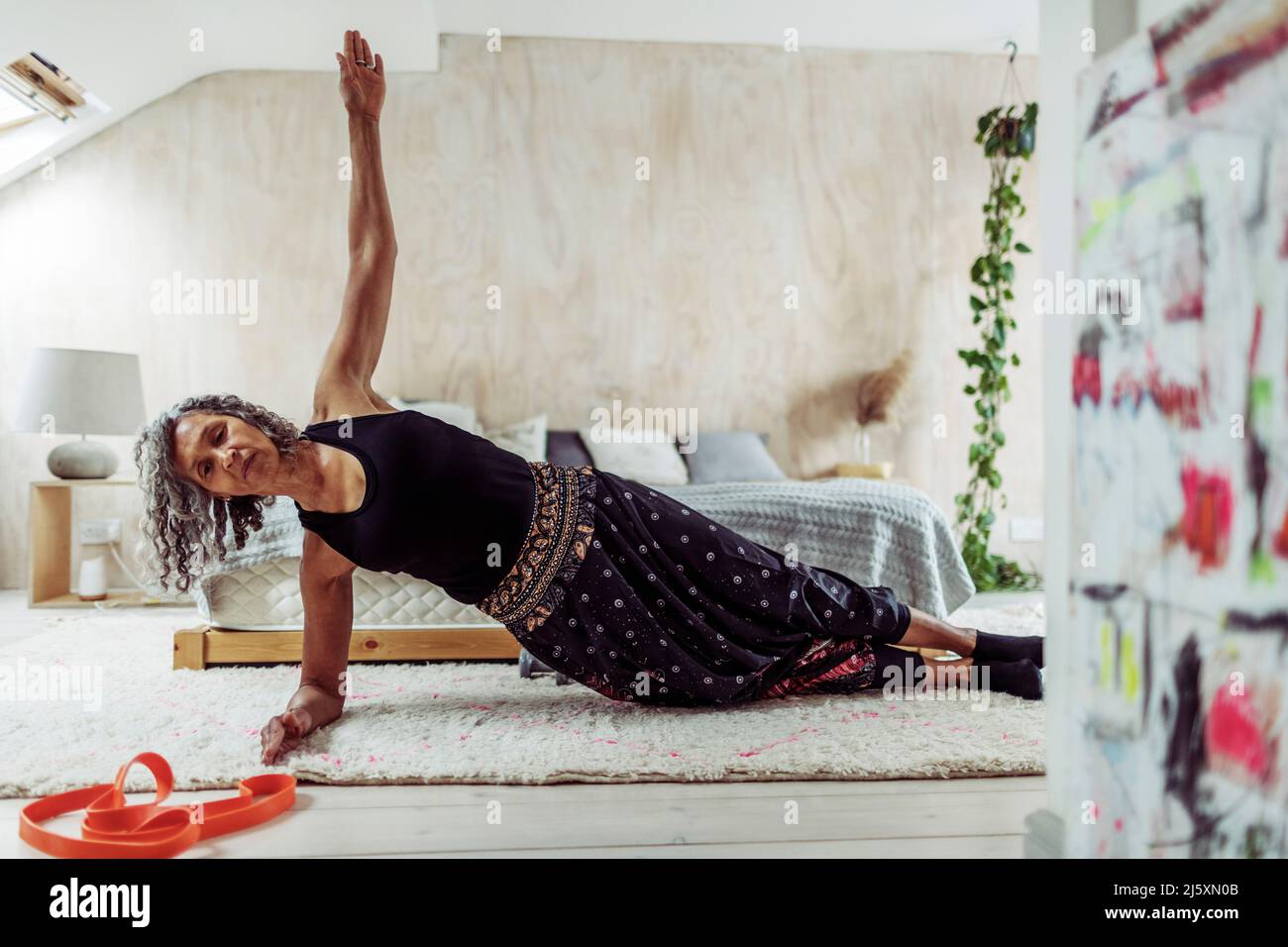 Senior woman exercising in side plank on bedroom rug Stock Photo