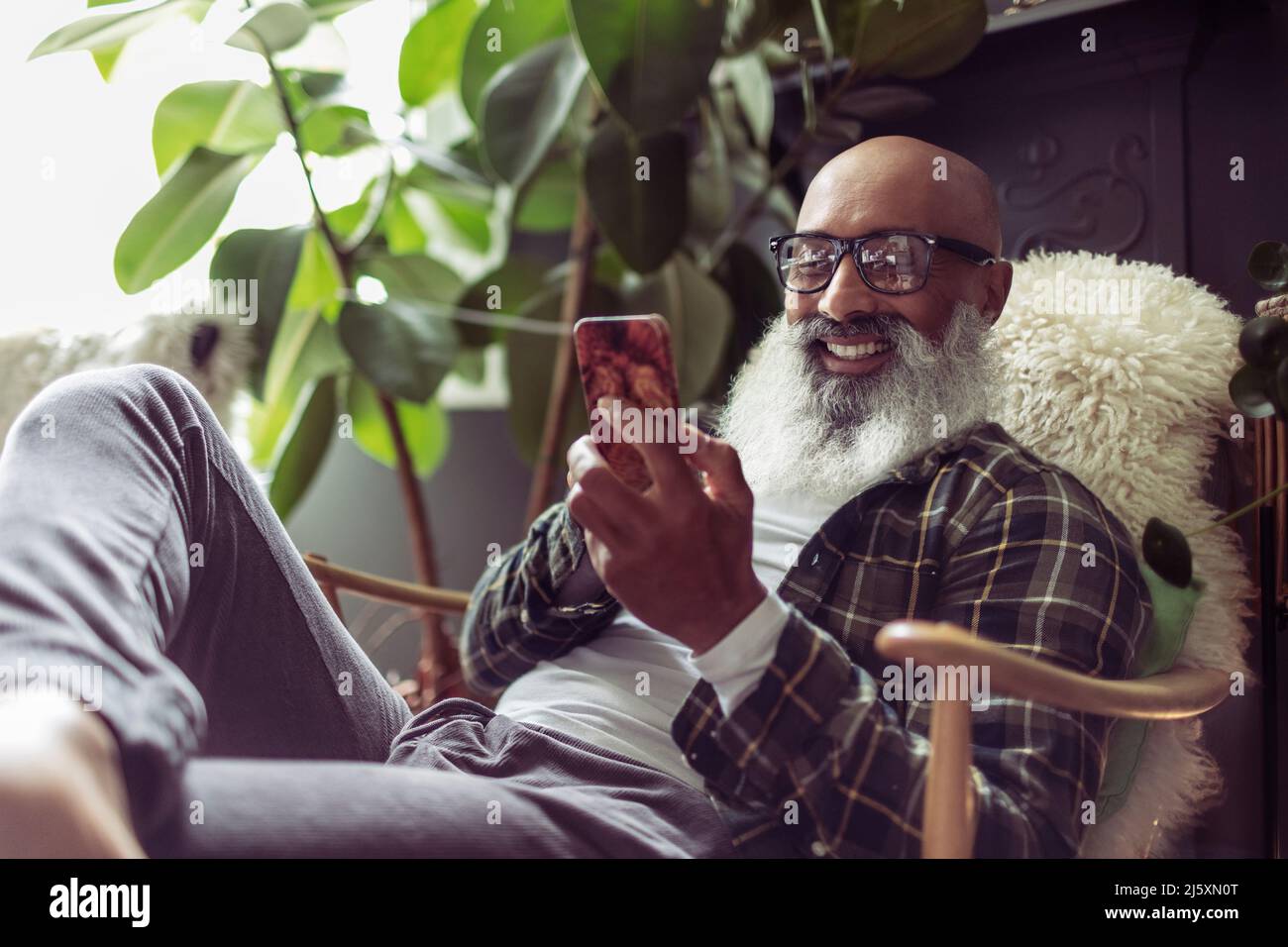 Happy senior man using smart phone in armchair Stock Photo