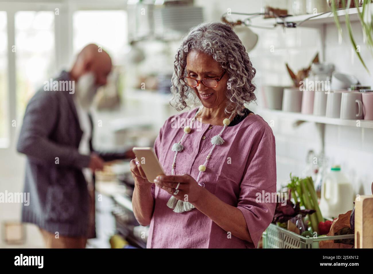 Senior woman using smart phone in kitchen Stock Photo