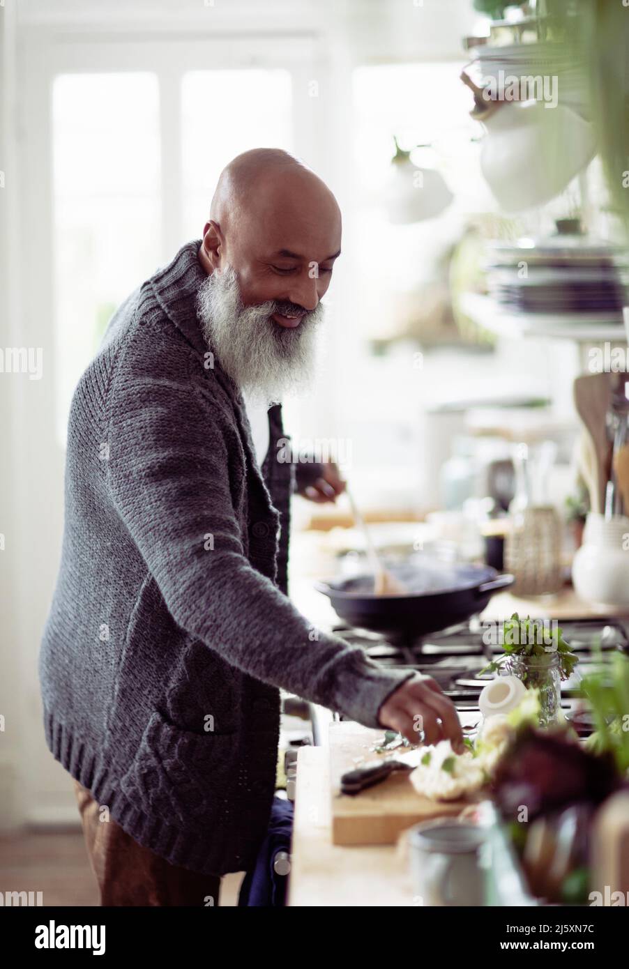 Smiling man with beard cooking in kitchen Stock Photo