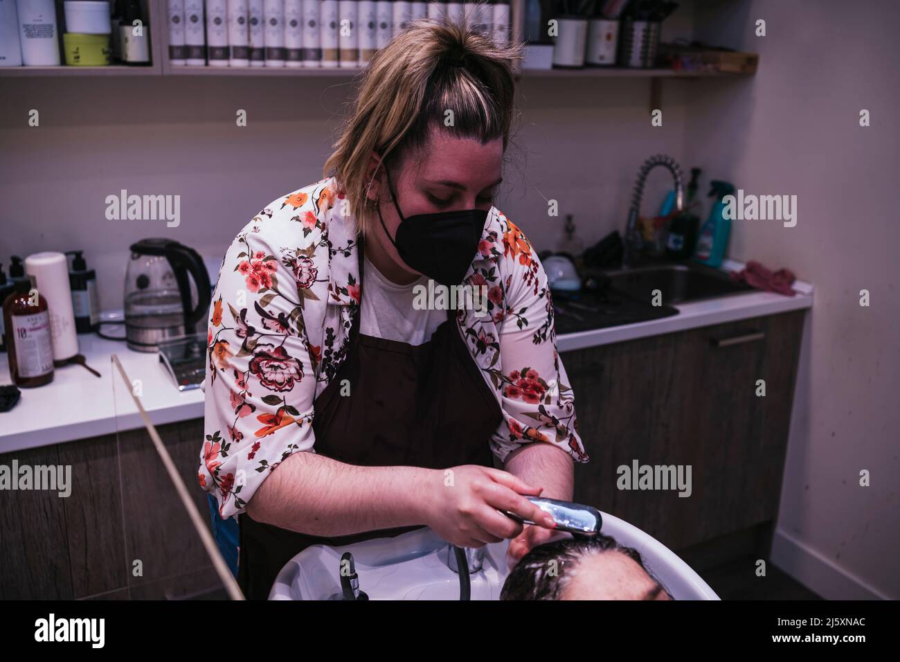 beautiful young woman enjoying a head massage with her eyes closed, while the professional hairdresser washes her hair with shampoo. Hairstylist worki Stock Photo