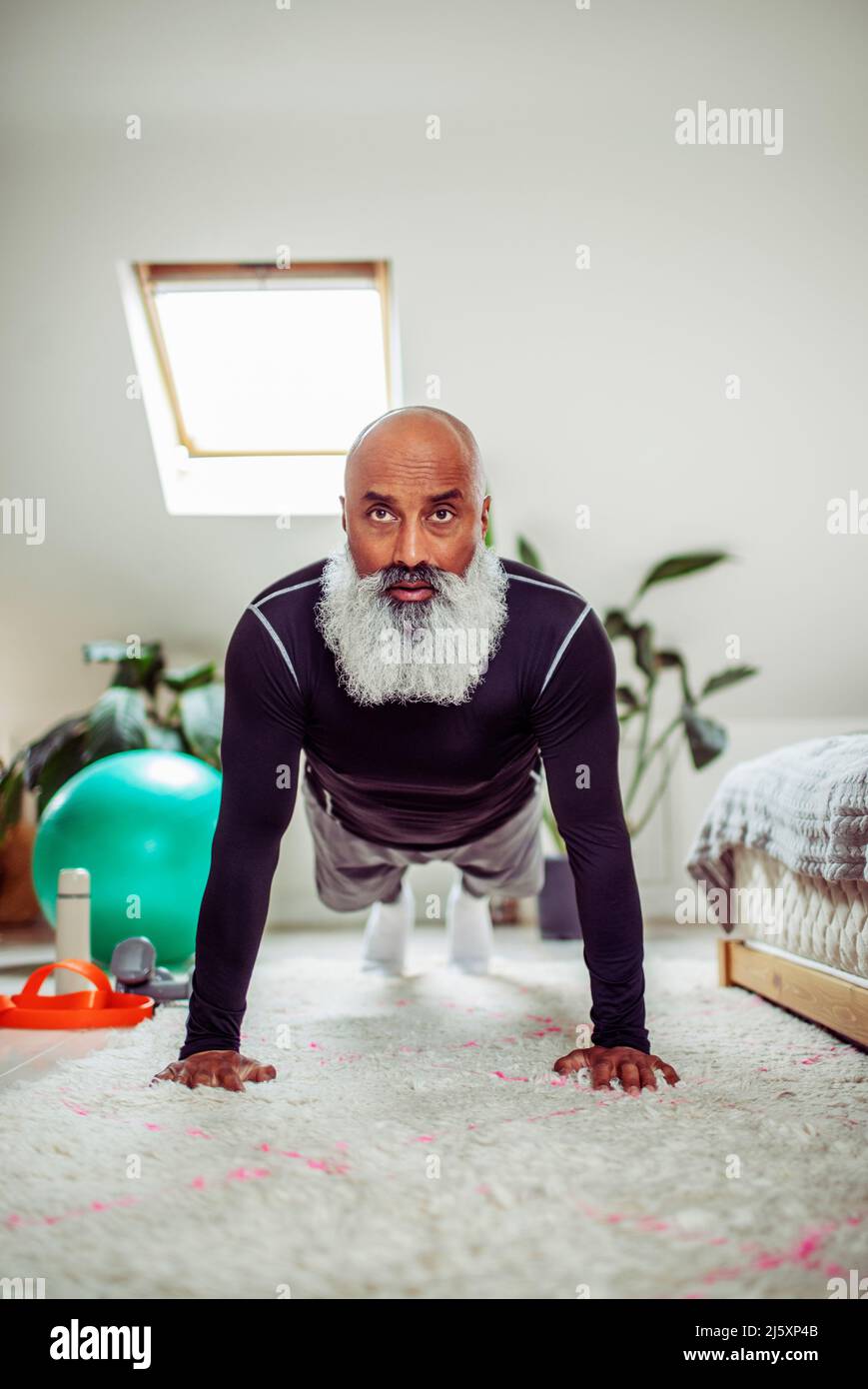 Focused mature man exercising in plank pose on bedroom floor Stock Photo