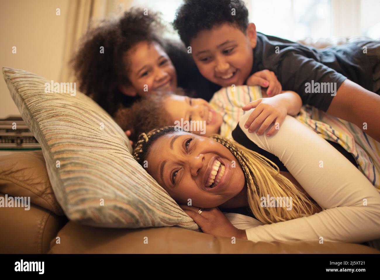 Happy playful mother and children cuddling on living room sofa Stock Photo