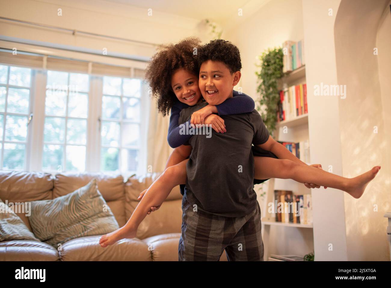 Portrait happy brother piggybacking sister in living room Stock Photo