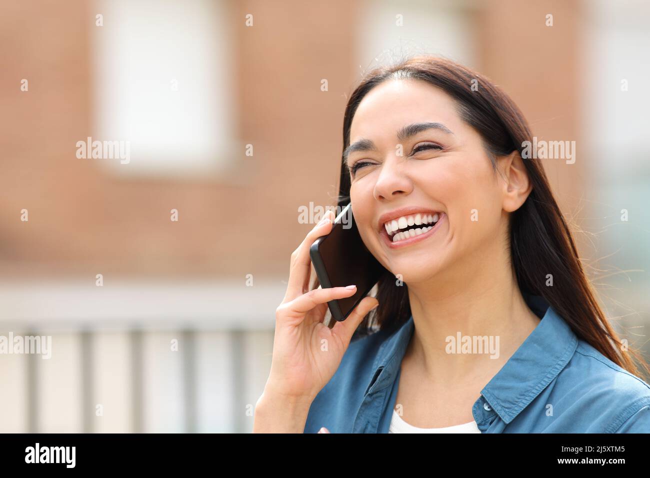 Happy woman laughing while is talking on phone walking in the street Stock Photo