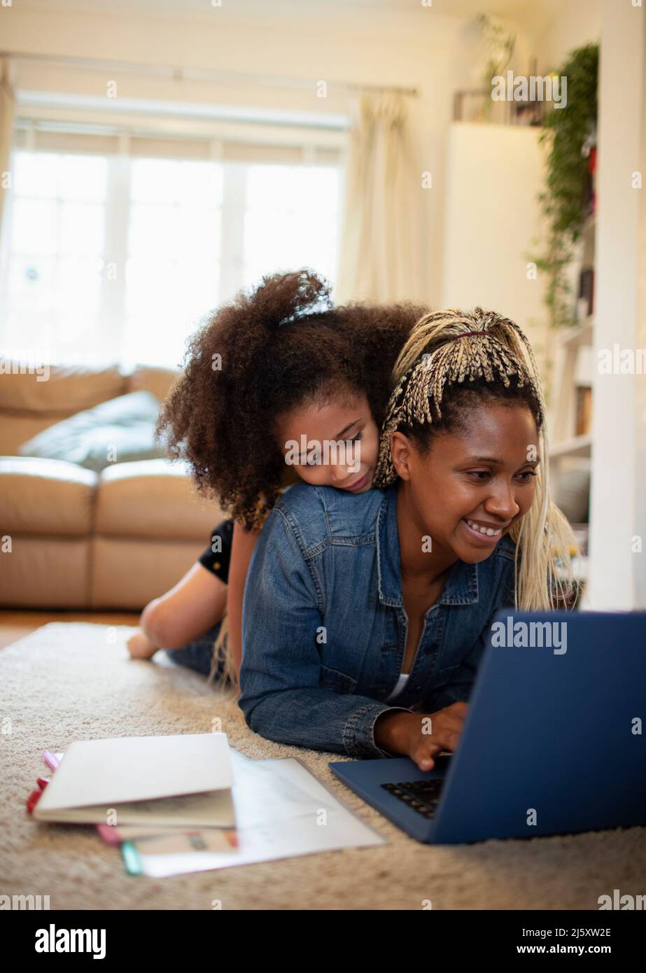 Curious girl watching mother work at laptop on living room floor Stock Photo