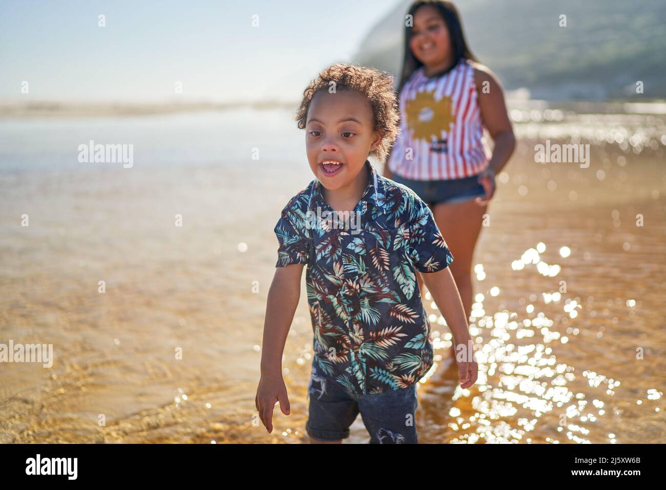 Happy brother with Down Syndrome and sister playing in sunny ocean Stock Photo