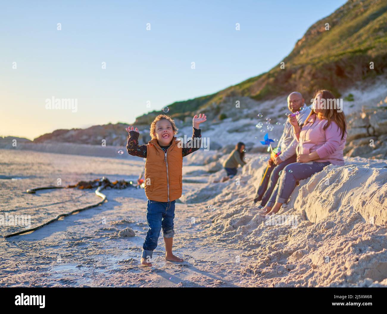 Happy boy with Down Syndrome playing with bubbles on sandy beach Stock Photo