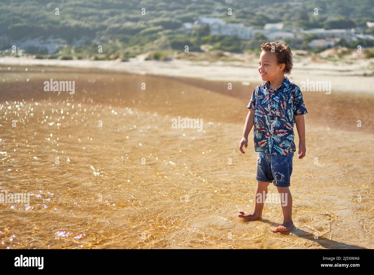 Happy boy with Down Syndrome wading in ocean surf on sunny beach Stock Photo
