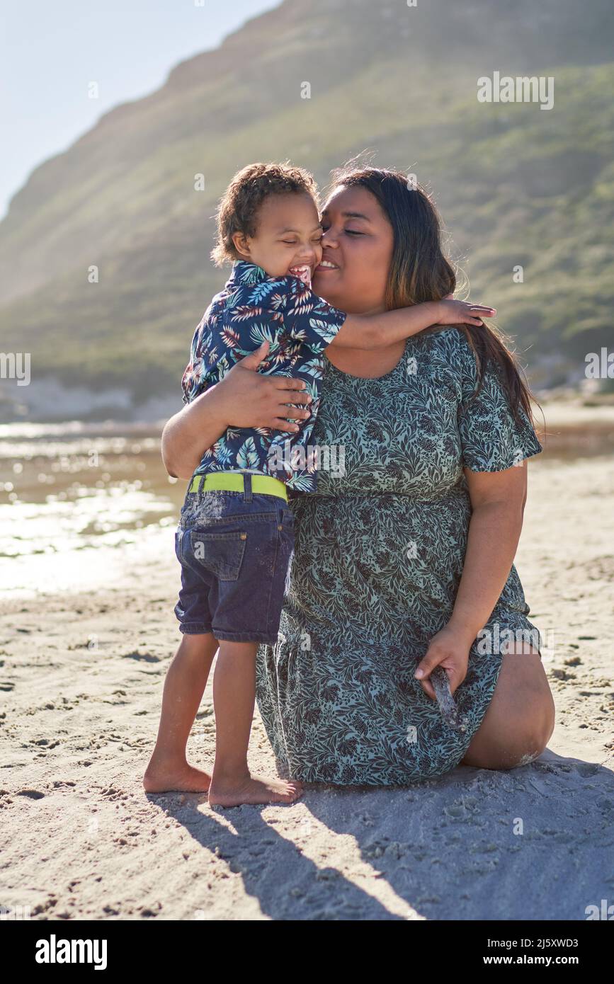 Affectionate mother hugging happy son on sunny beach Stock Photo