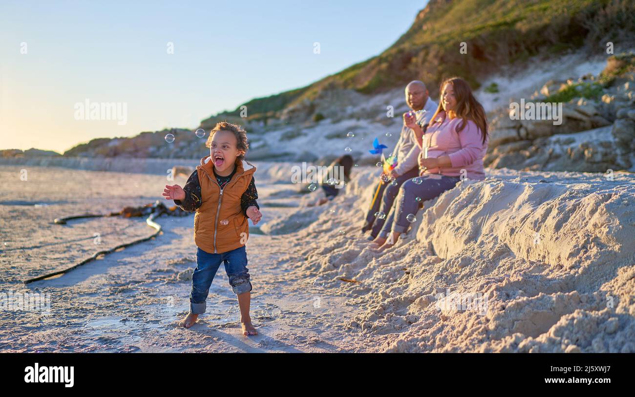 Cute boy with Down Syndrome playing with bubbles on beach Stock Photo