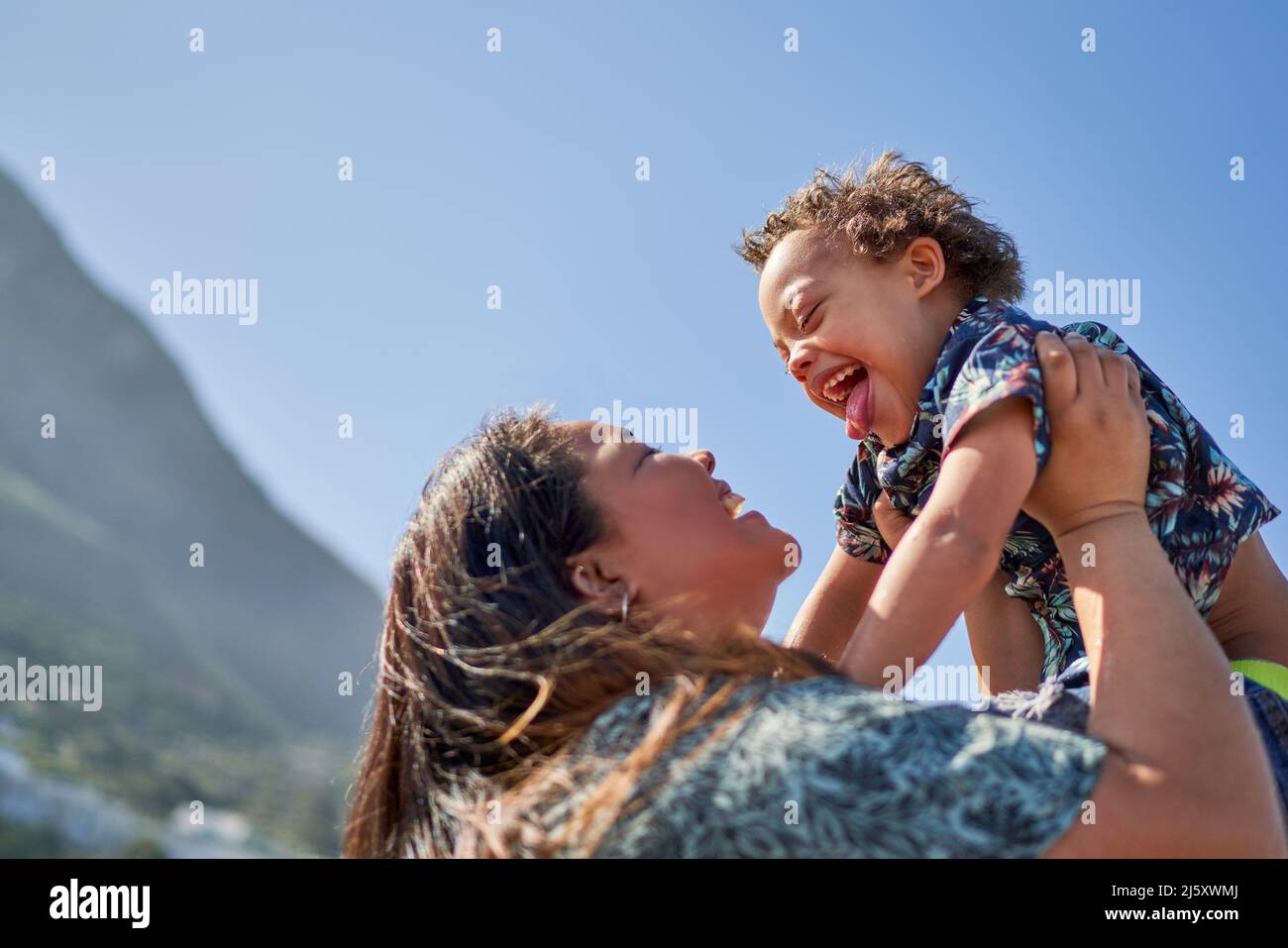 Happy mother lifting son with Down Syndrome below sunny blue sky Stock Photo