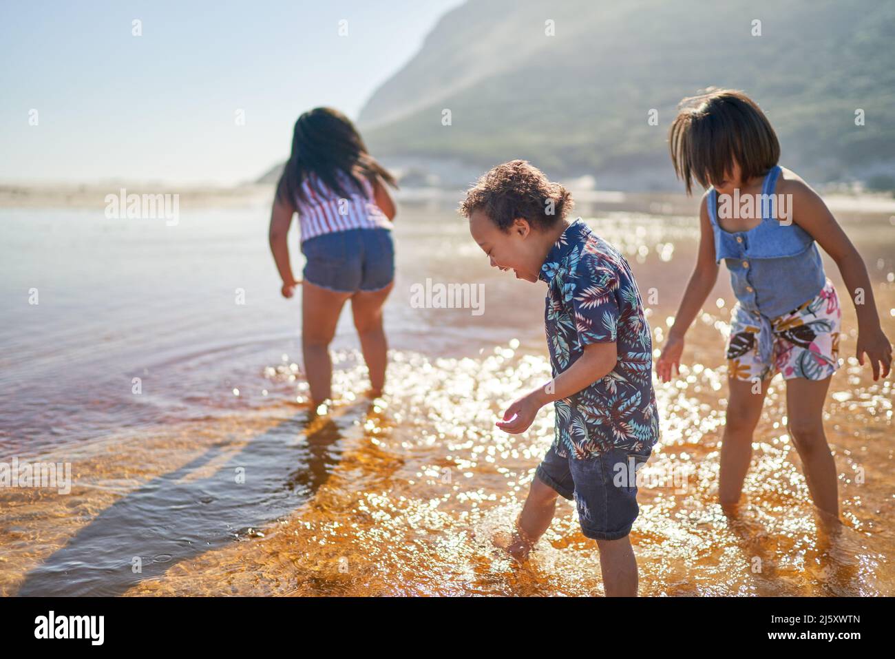 Boy with Down Syndrome and sisters wading in sunny ocean Stock Photo