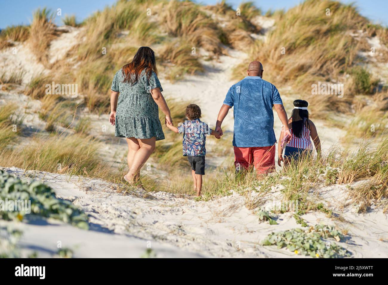 Family holding hands and walking on sandy beach path Stock Photo