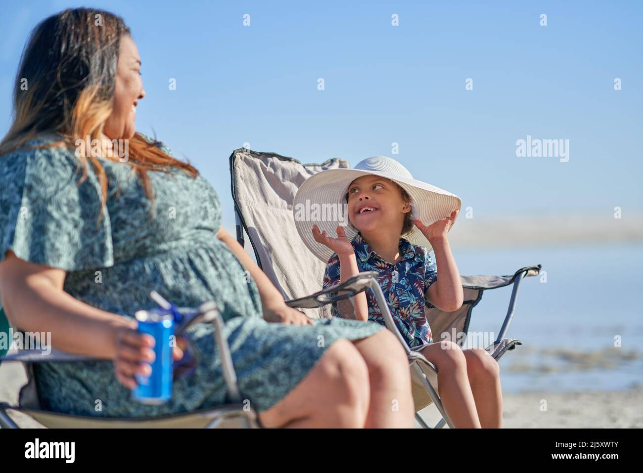 Mother watching happy cute son with Down Syndrome in hat on beach Stock Photo