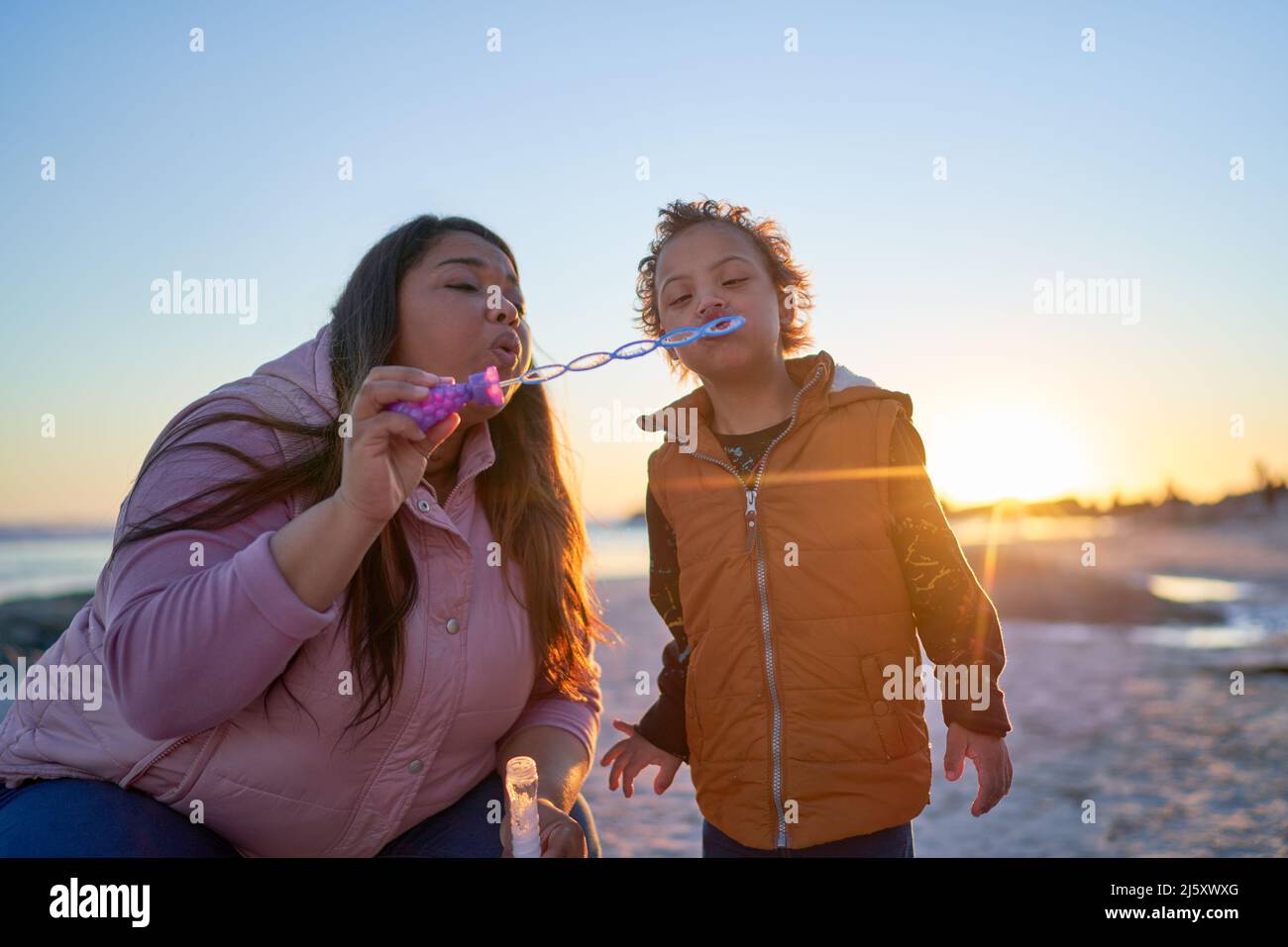 Mother and son with Down Syndrome blowing bubbles on beach Stock Photo