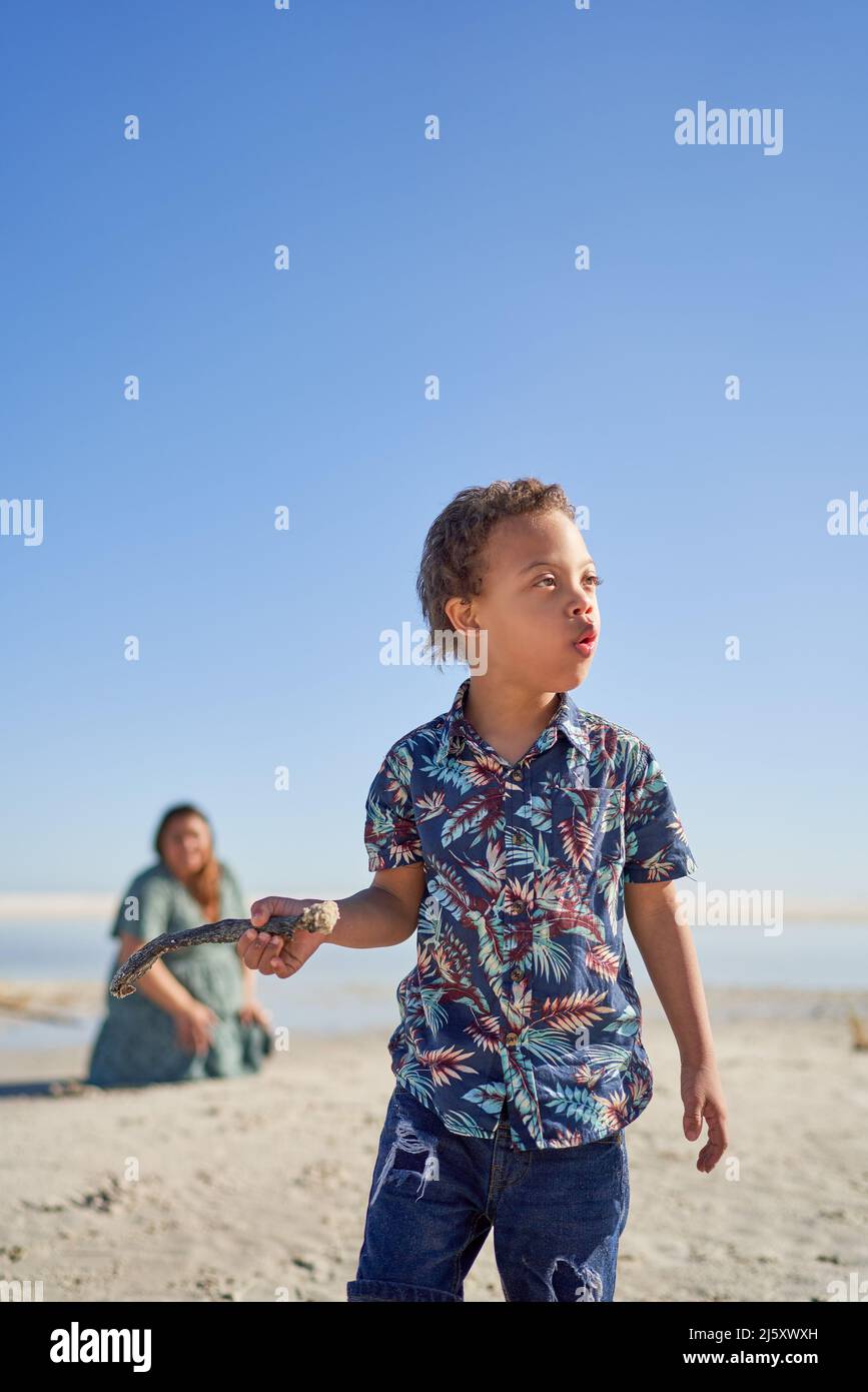 Boy with Down Syndrome holding stick on sunny beach Stock Photo