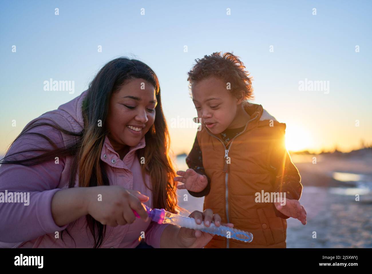 Happy mother and son with Down Syndrome playing with bubbles on beach Stock Photo
