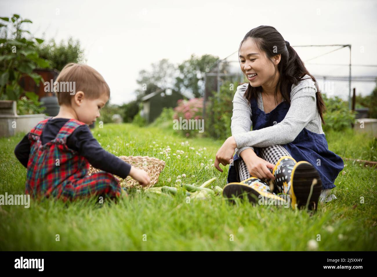 Happy mother watching son with vegetables in garden grass Stock Photo