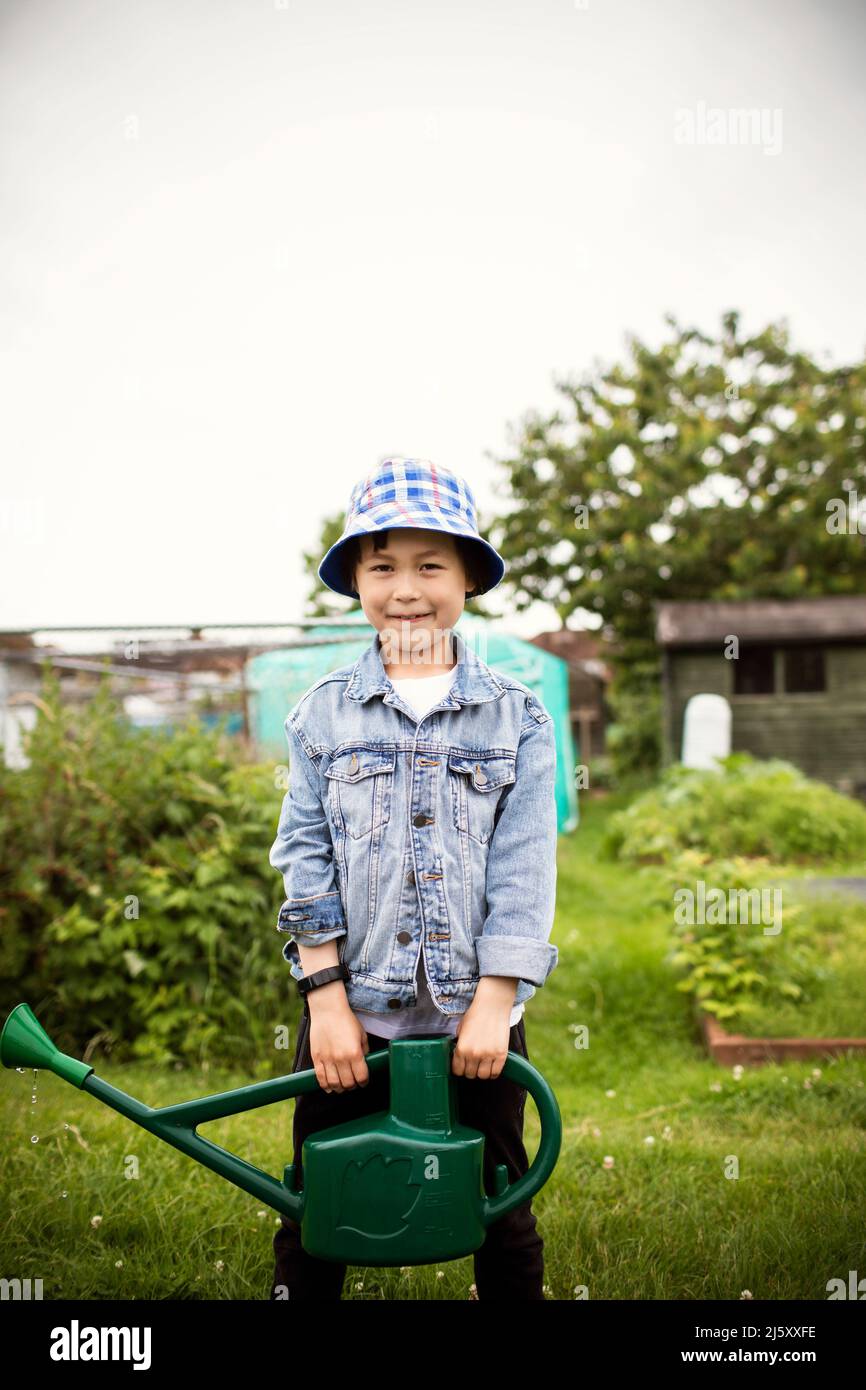 Portrait smiling boy with watering can in vegetable garden Stock Photo