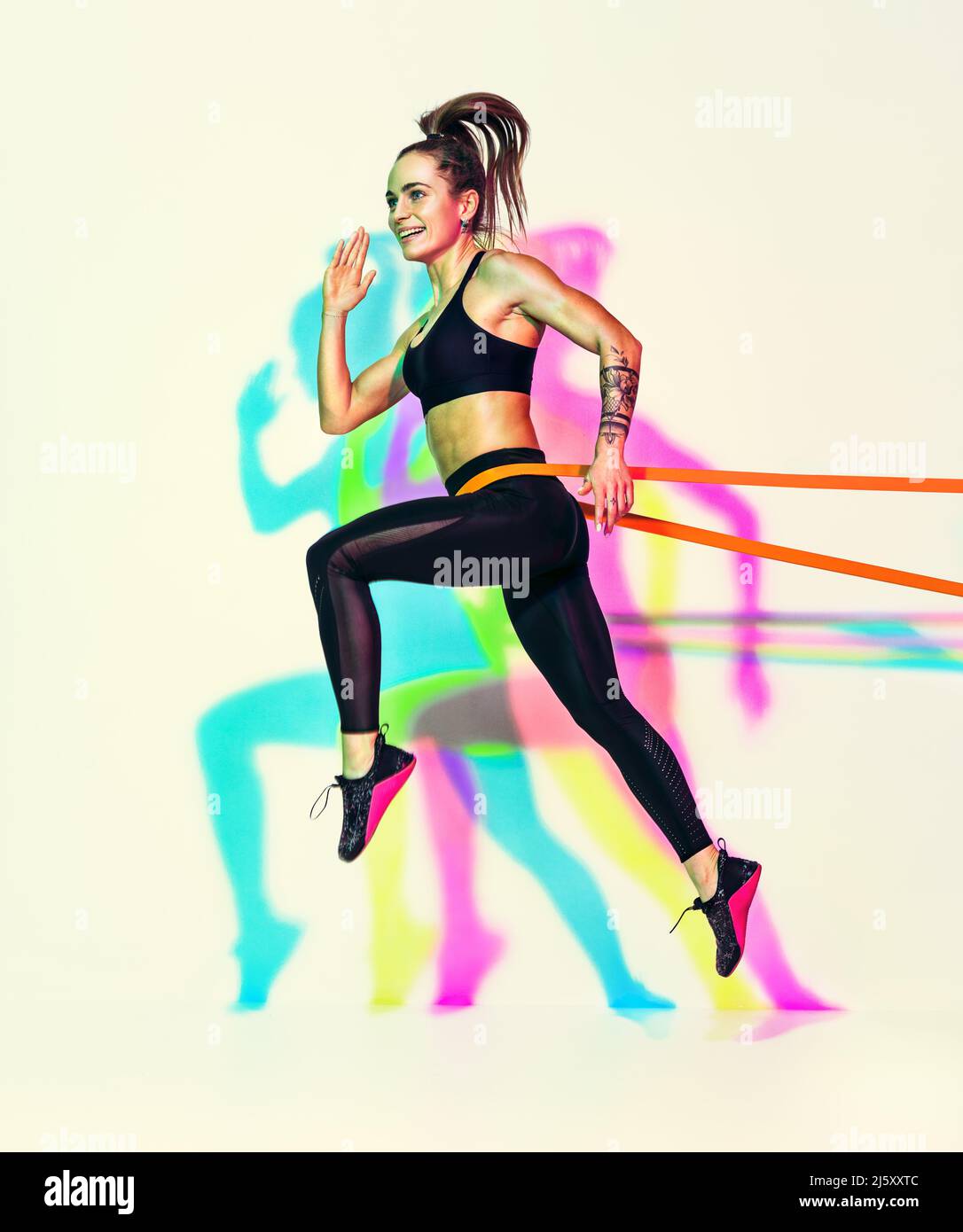 Sporty woman doing jumping exercise with resistance band. Photo of muscular woman in black sportswear on white background with effect of rgb colors sh Stock Photo