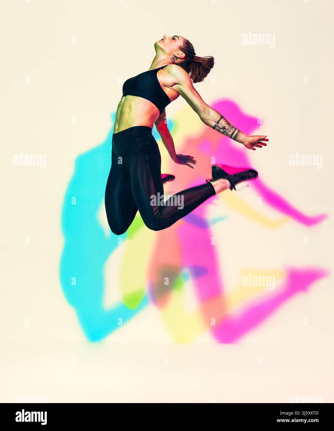 Sporty woman jumping up in silhouette. Photo of muscular woman in black sportswear on white background with effect of rgb colors shadows. Dynamic move Stock Photo