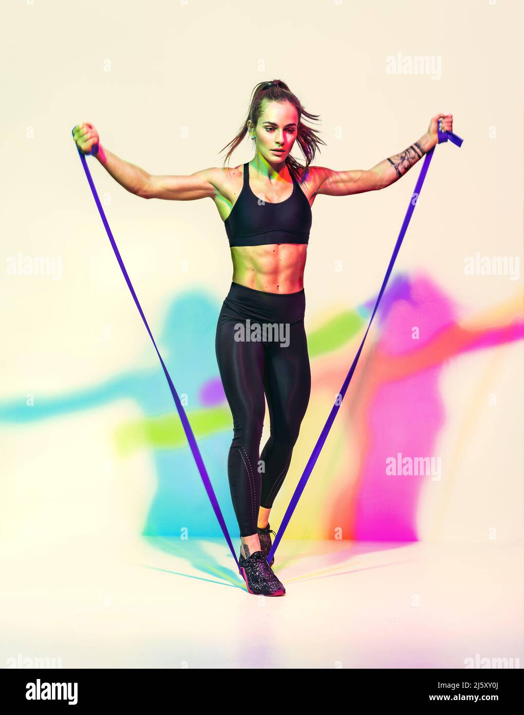 Strong woman working with resistance band. Photo of woman in black sportswear on white background with effect of rgb colors shadows. Sports and health Stock Photo