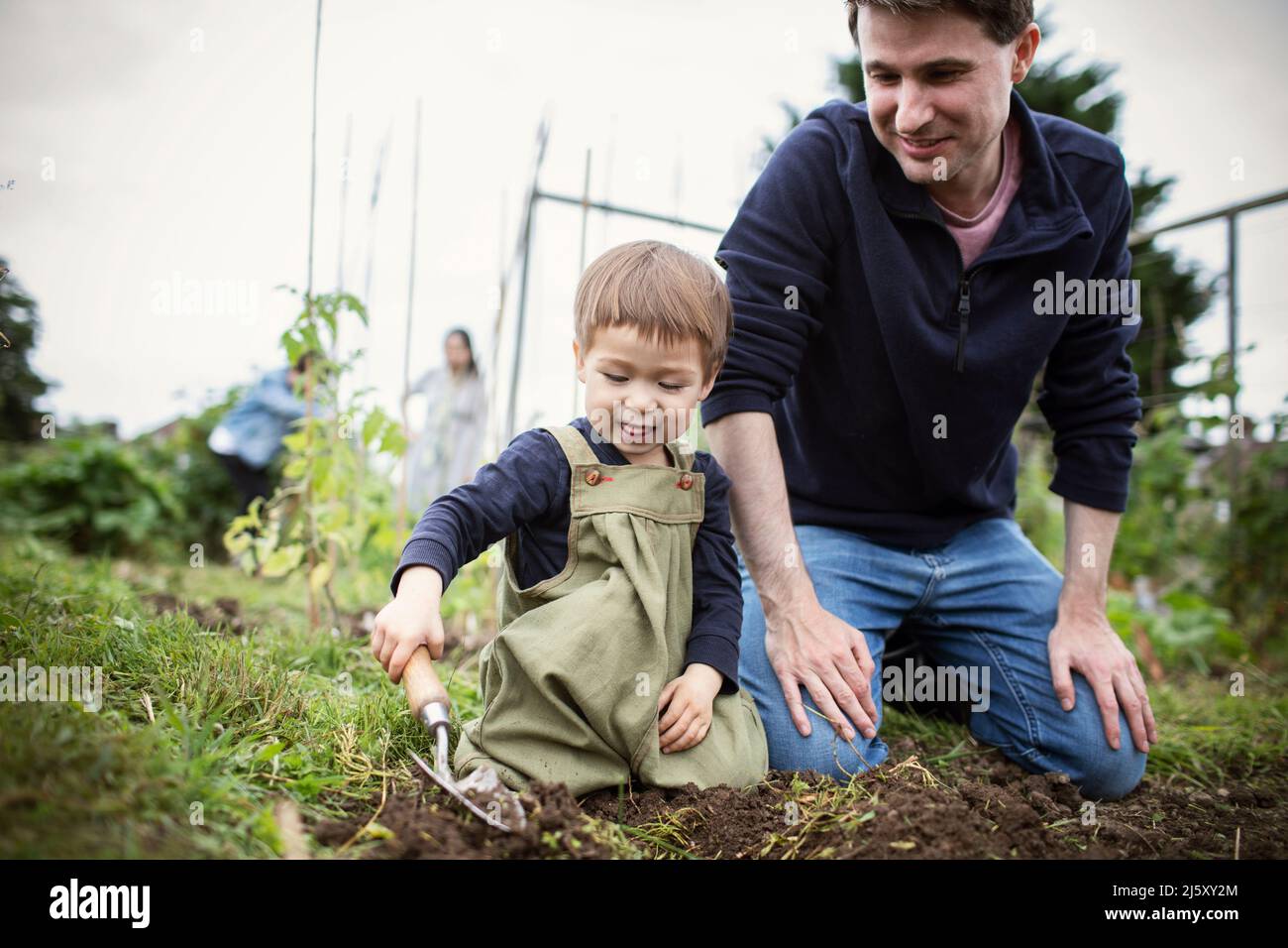 Father and son digging in garden dirt with trowel Stock Photo