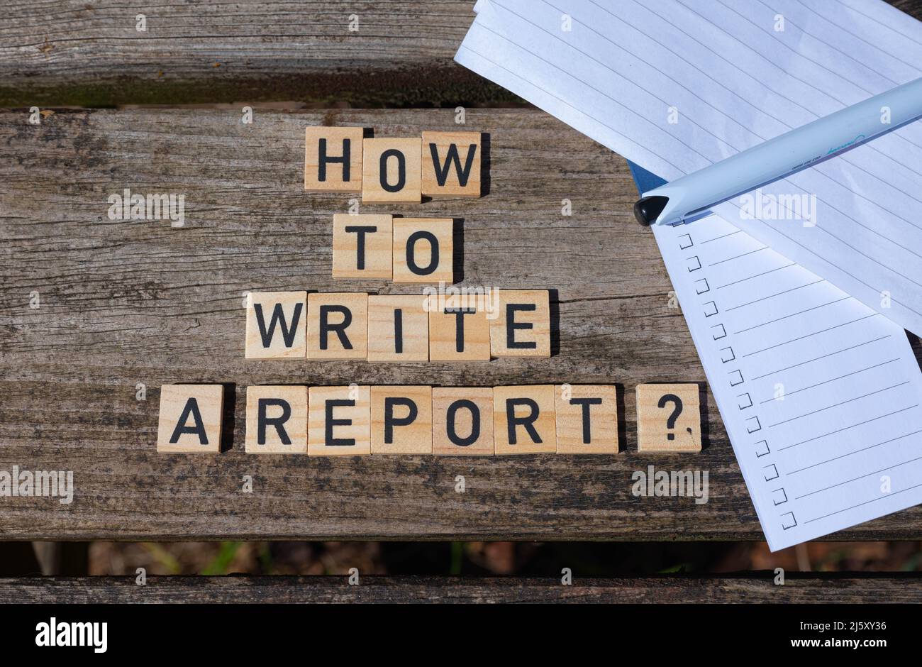 How to write a report? Black capital letter words on wooden toy blocks on a natural garden table background with paper and pencil. Stock Photo