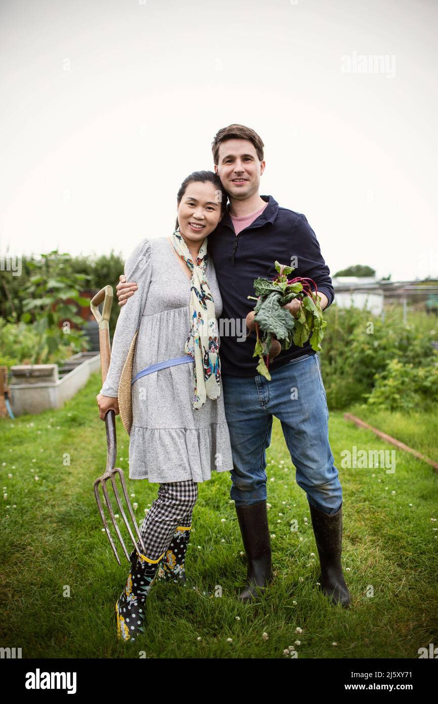 Portrait happy couple with harvested vegetables in garden Stock Photo