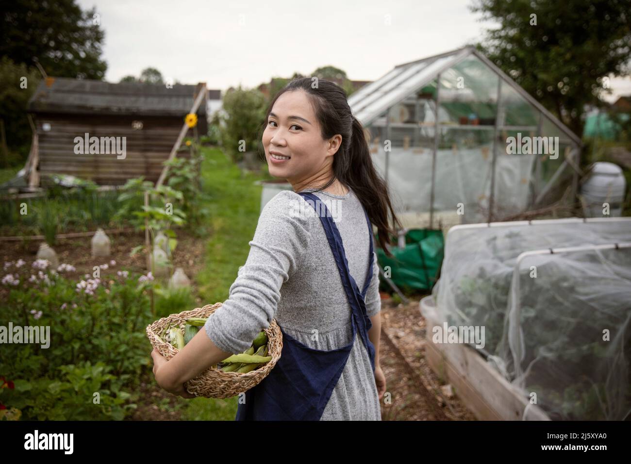 Portrait happy woman with basket of harvested vegetables in garden ...