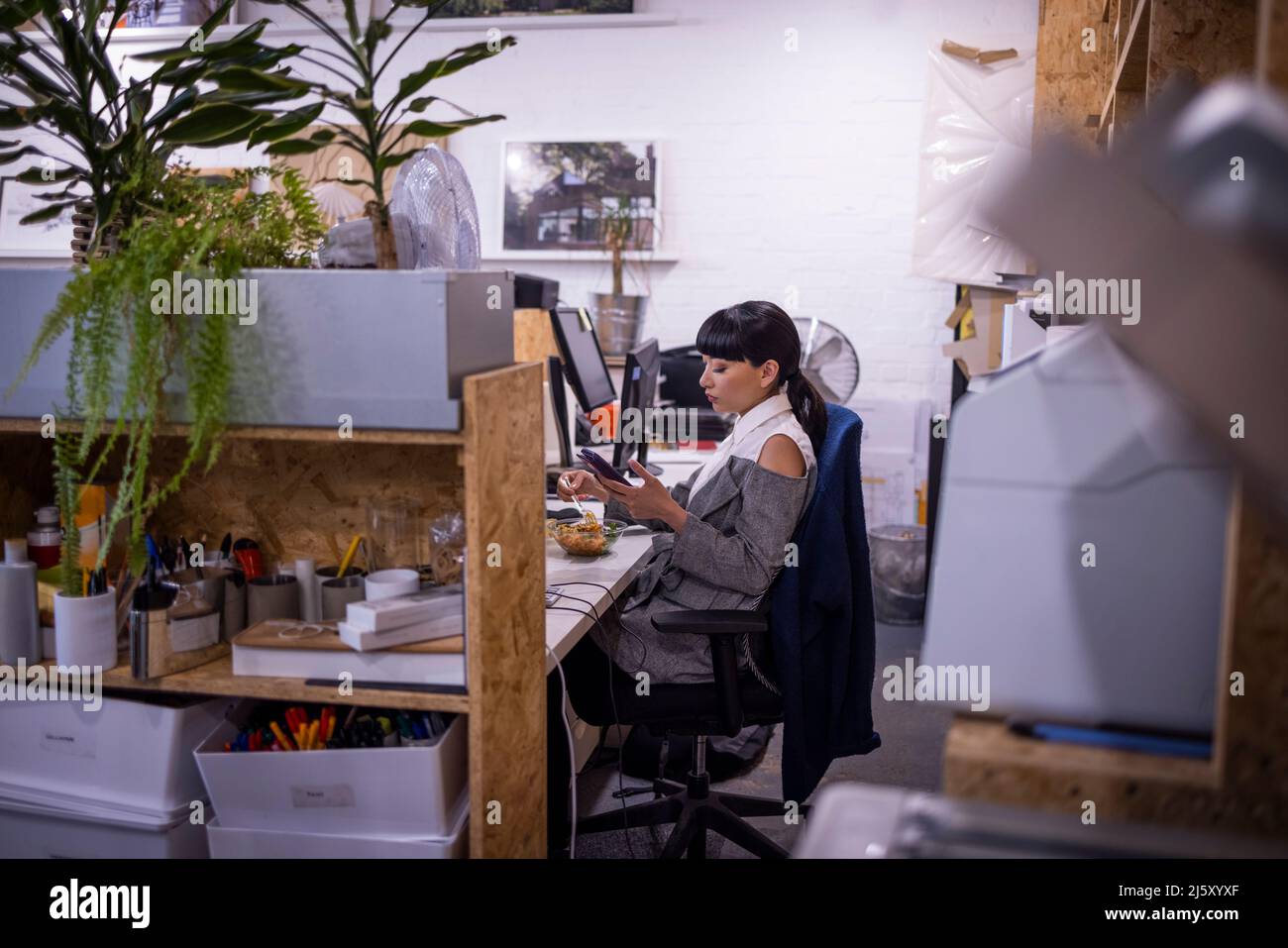 Businesswoman using smart phone at desk in creative office Stock Photo