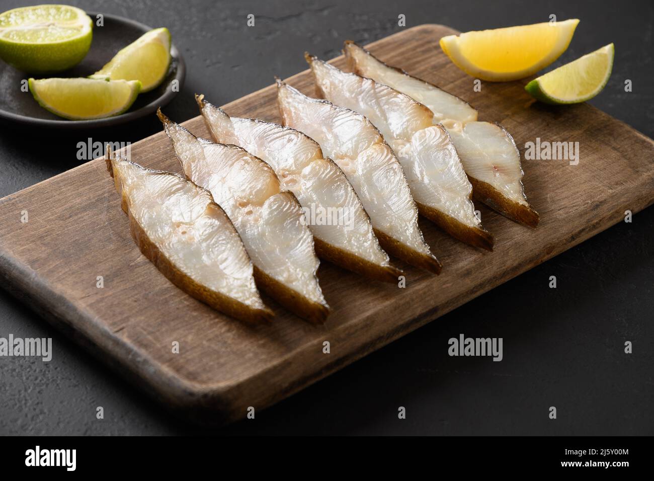 Delicious smoked halibut slices served with lime on black background. Close up. Copy space. Stock Photo