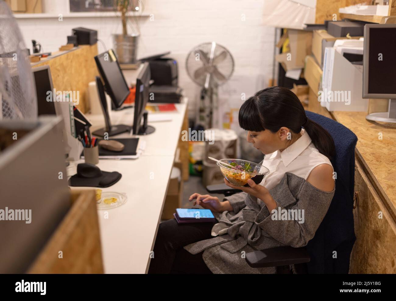 Businesswoman eating lunch and using smart phone in office Stock Photo