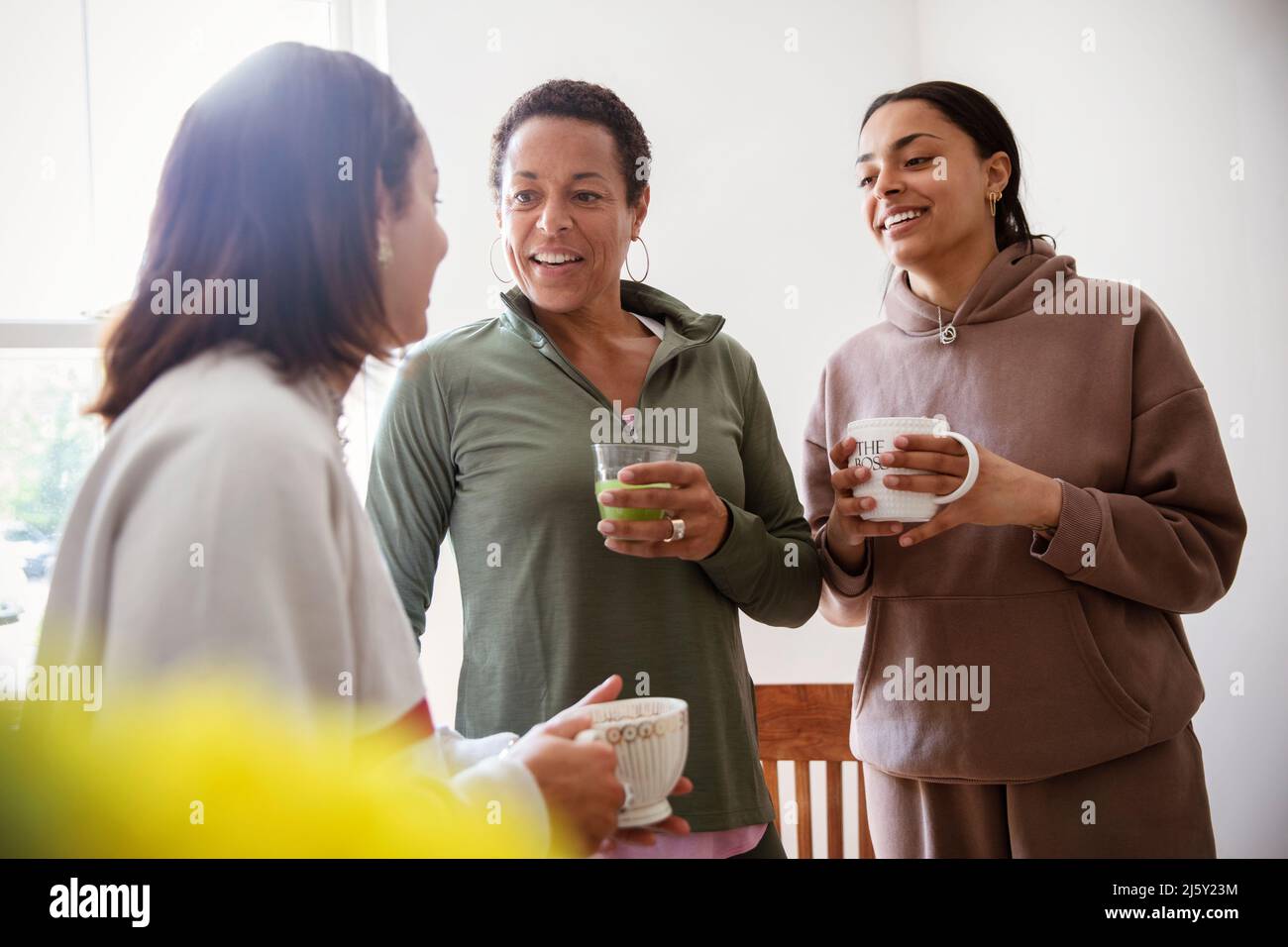 Mother and young adult daughters talking and drinking at home Stock Photo