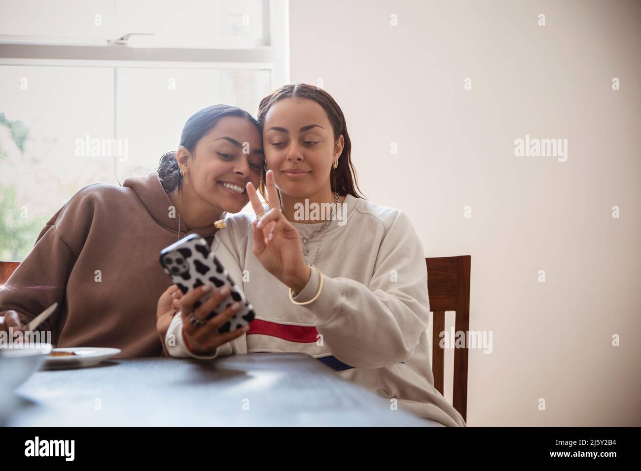 Smiling, cool young adult sisters taking selfie with smart phone Stock Photo