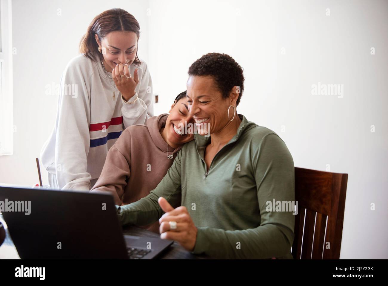 Happy mother and daughters using laptop in dining room Stock Photo