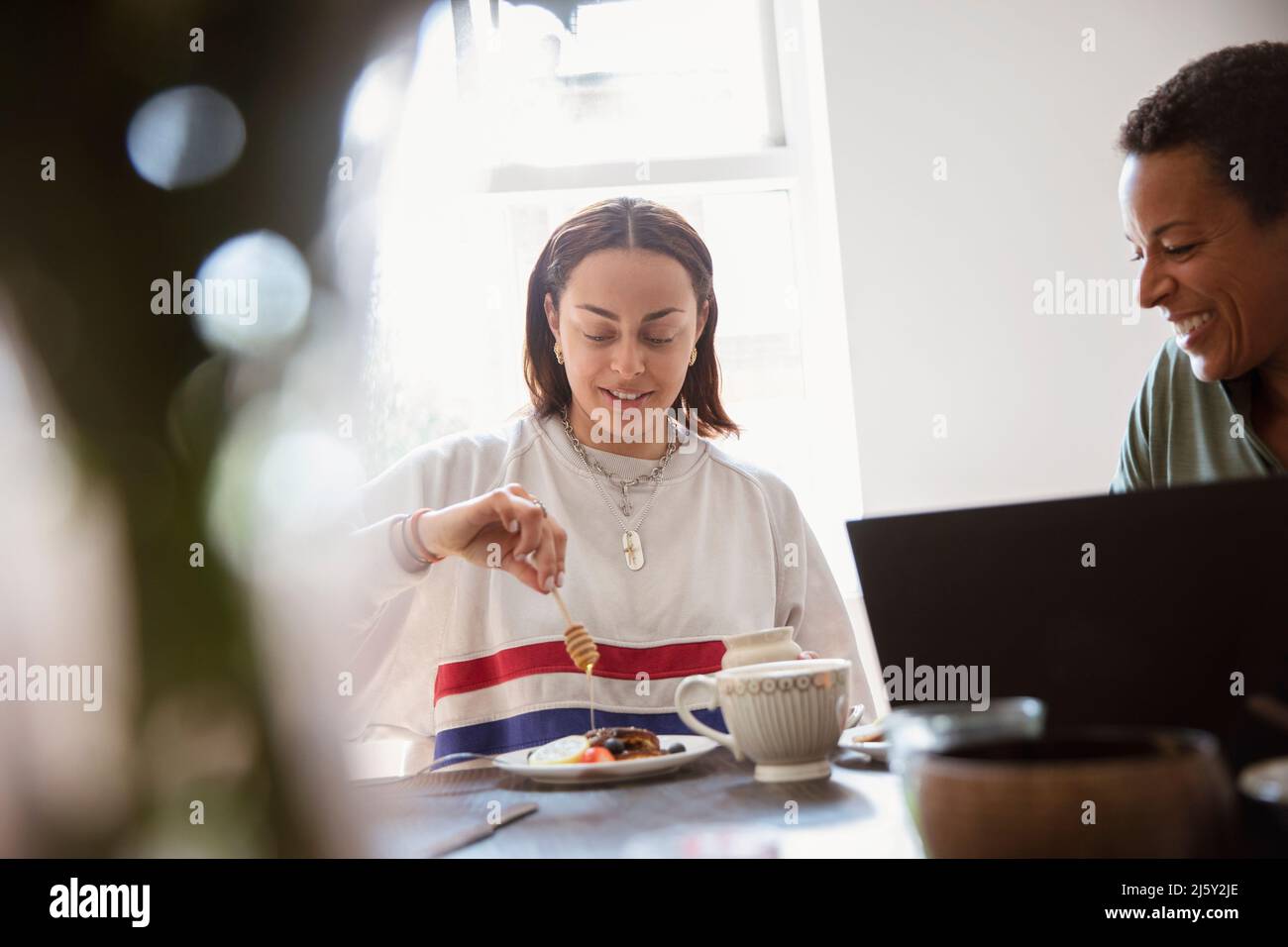 Young woman drizzling honey over breakfast at dining table Stock Photo