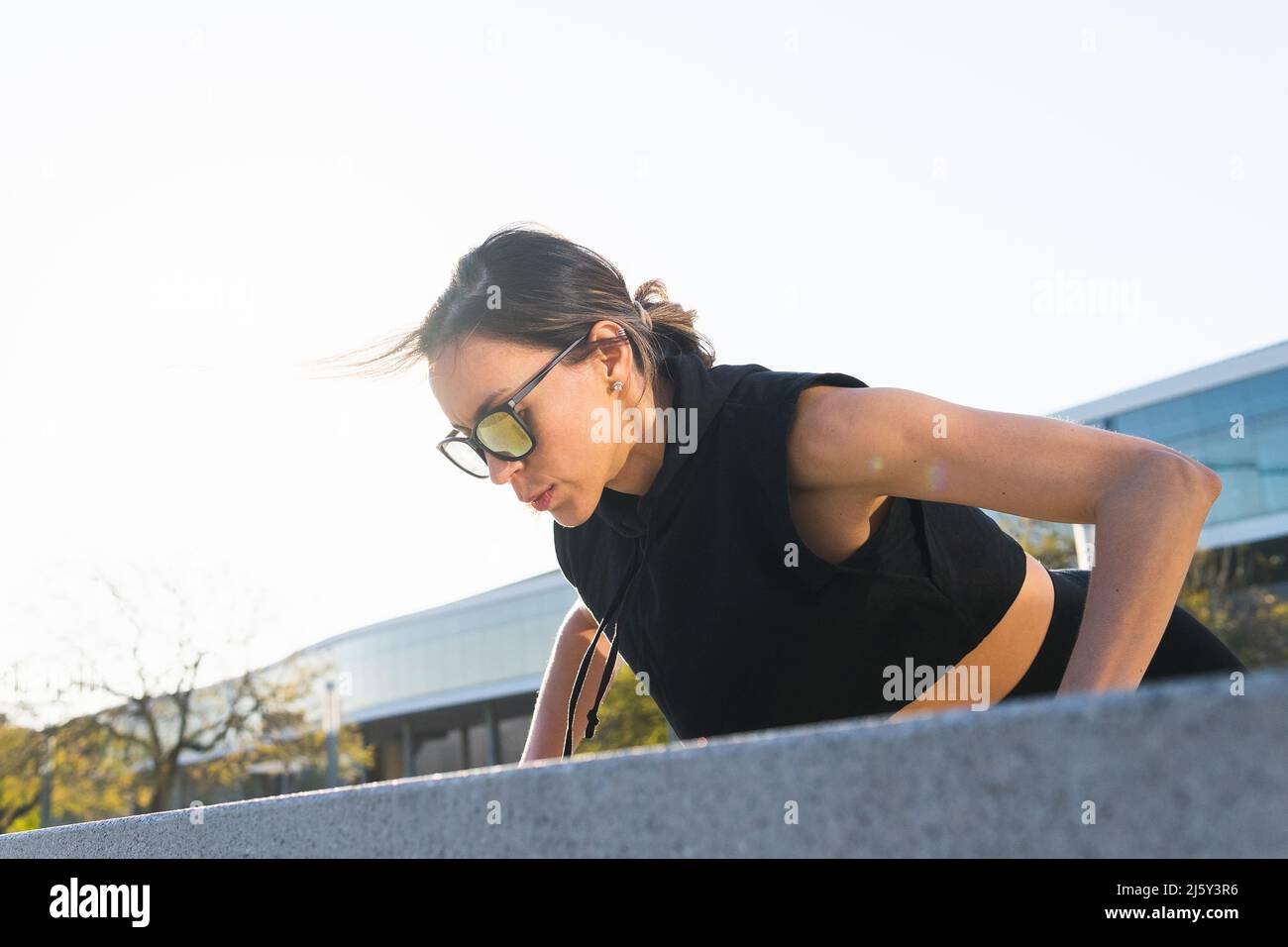 Low angle of strong female athlete in sunglasses and activewear doing