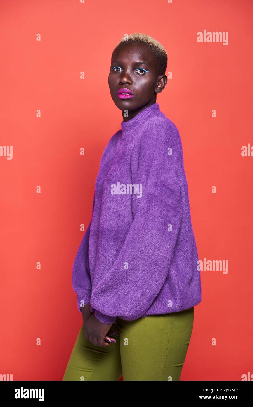 Side view of a pleasant African Woman with short hair in a studio shot with a red background Stock Photo