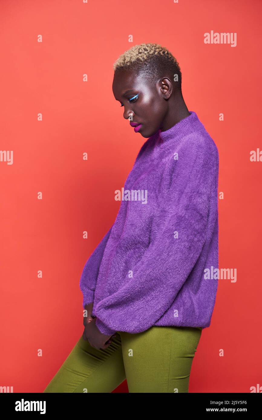 Side view of a pleasant African Woman with short hair in a studio shot with a red background Stock Photo
