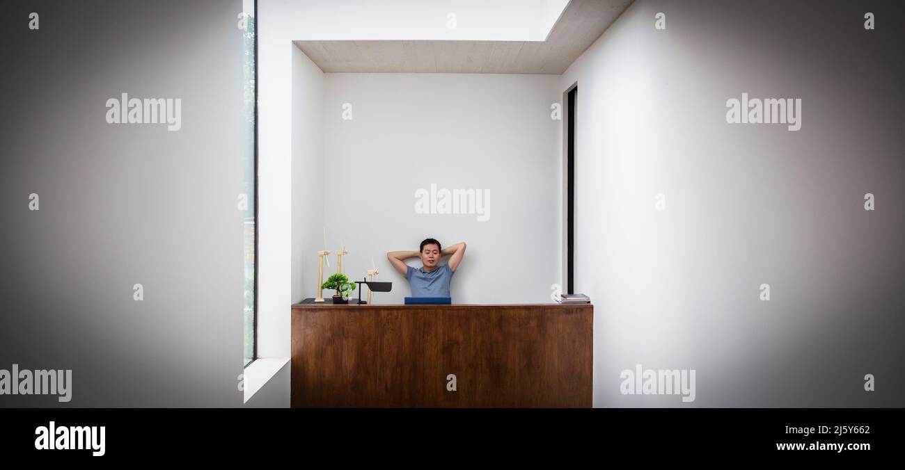 Male engineer with hands behind head at desk with wind turbine models Stock Photo