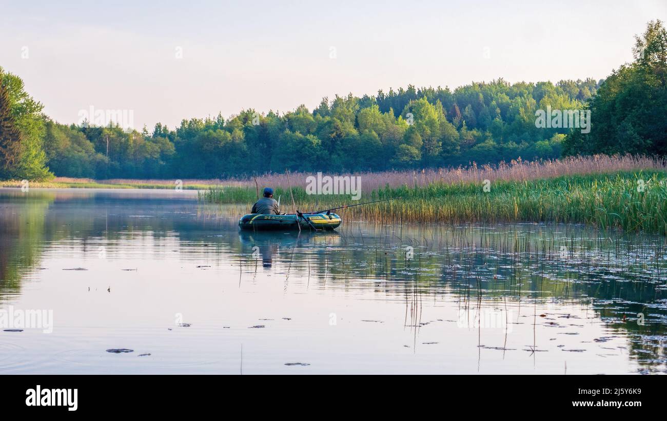 Minsk region, Belarus - June 09, 2020: Fisherman on a boat in the early morning on a lake fishing in the reeds Stock Photo